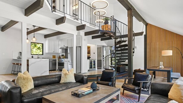 A spacious living area with a black leather sofa, a wooden coffee table, and a patterned rug. A staircase with a black railing leads to an upper level. - Lake Daze in Kings Beach (Kings Beach)