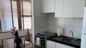 A modern kitchen with white cabinets, a black countertop, and a window with blinds.