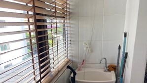 A small bathroom with a window, a sink, and cleaning tools.