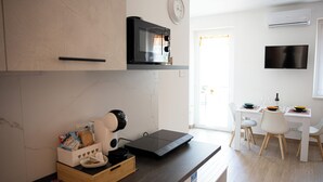 A modern kitchen with a microwave, toaster, and coffee machine on the counter. There is a dining area with a table and chairs. - BEIGE APARTAMENT (Gragnano)