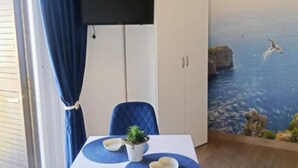 Quarto com mesa de jantar, cadeiras, planta em vaso e um mural de paisagem marítima.