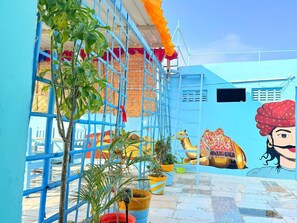 A vibrant outdoor area with a blue wall, potted plants, and a mural featuring a camel and a man.