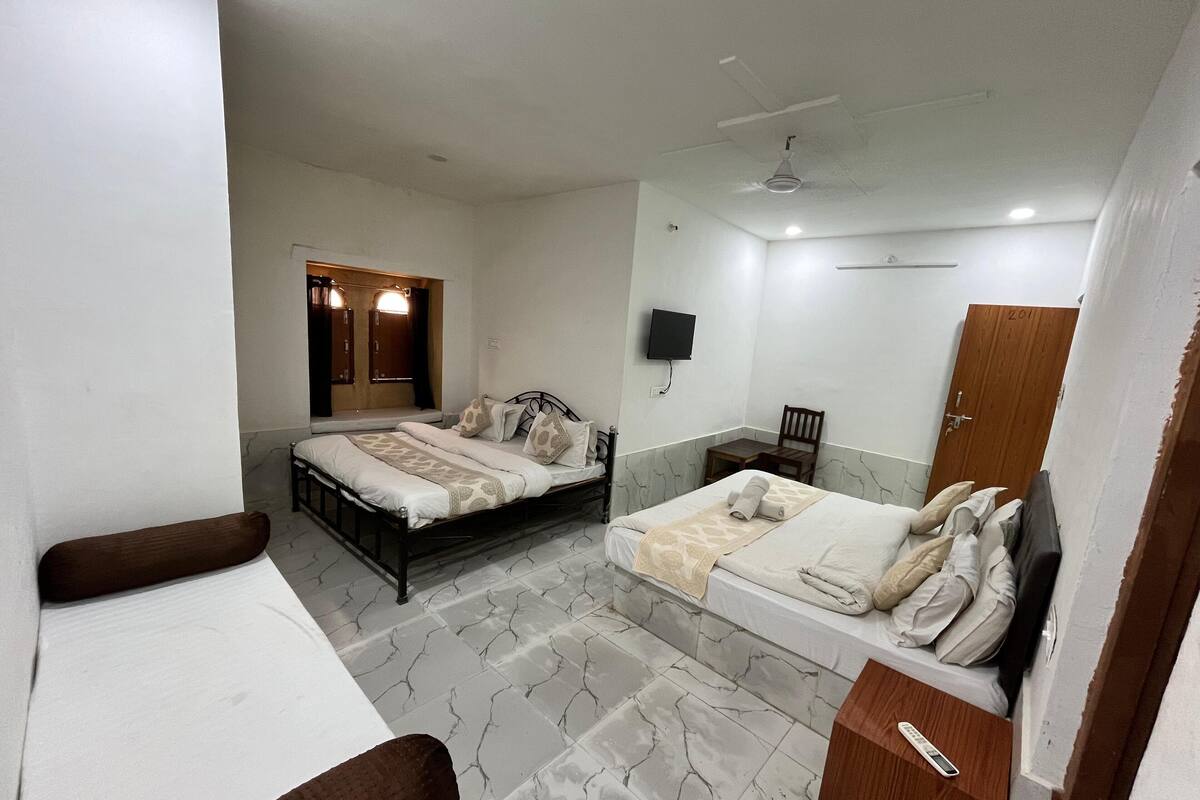 A bedroom with two beds, a TV, a wooden door, and a small table.