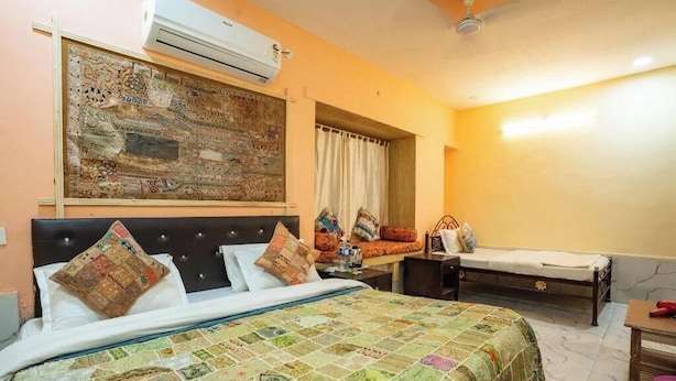 Un dormitorio con una cama, un banco, aire acondicionado y una obra de arte en la pared.