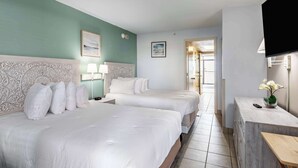 A hotel room with two beds, a TV, a desk with a vase of flowers, and a door leading to another room. - Sky-High Oceanfront Stay Pools and DJs & More (Myrtle Beach)