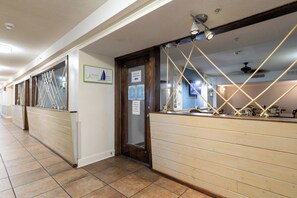 A hotel corridor with wooden paneling, a reception desk with rope decorations, and a sign indicating the use of another door.