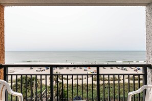 A balcony with a view of a beach, palm trees, and a sandy shore. - Sky-High Oceanfront Stay Pools and DJs & More (Myrtle Beach)