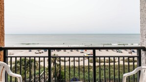 A balcony with a view of a beach, palm trees, and a sandy shore. - Sky-High Oceanfront Stay Pools and DJs & More (Myrtle Beach)