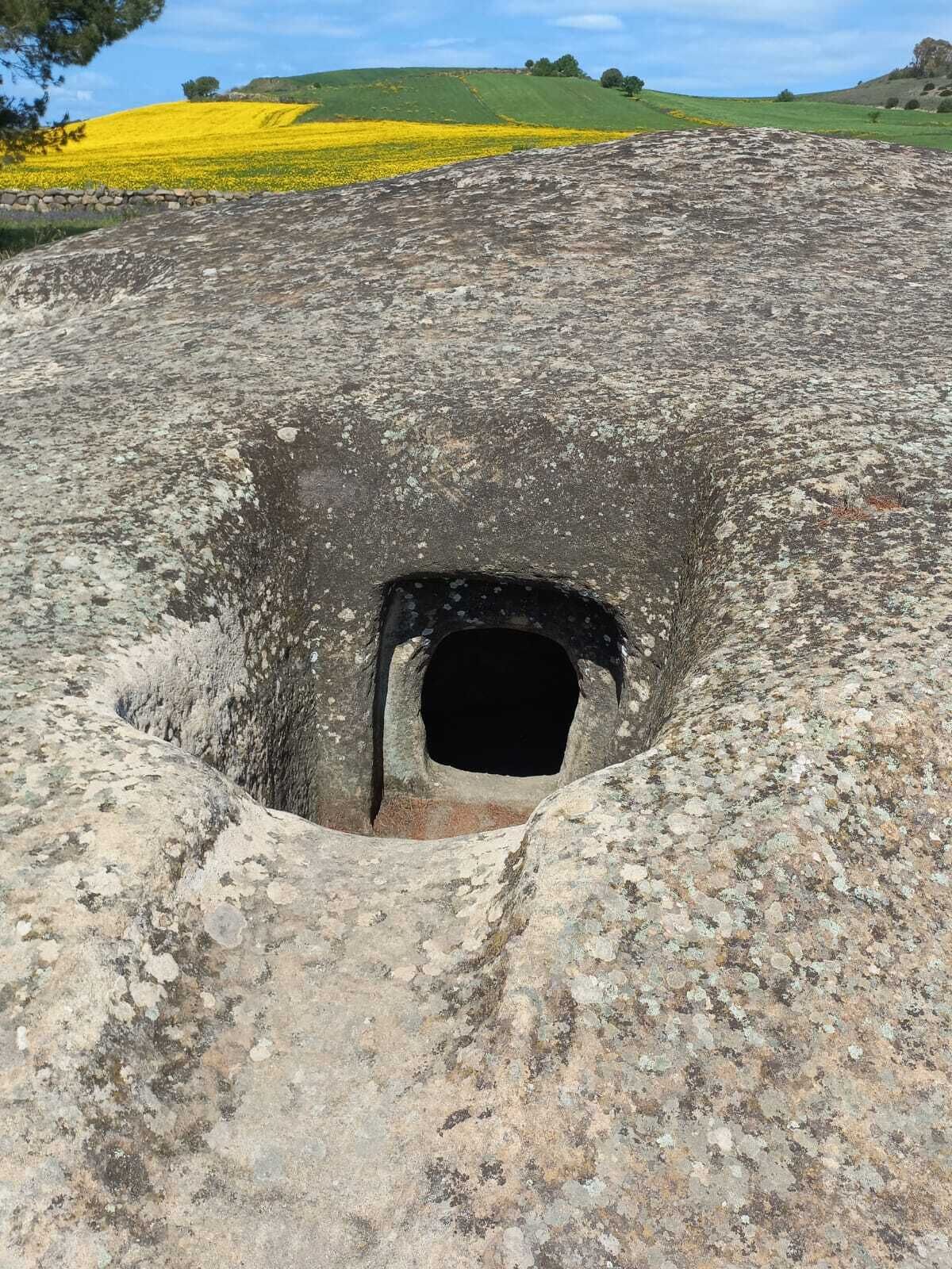 Une vaste structure circulaire en pierre, dotée d’une ouverture centrale et entourée d’un terrain accidenté et rocheux.