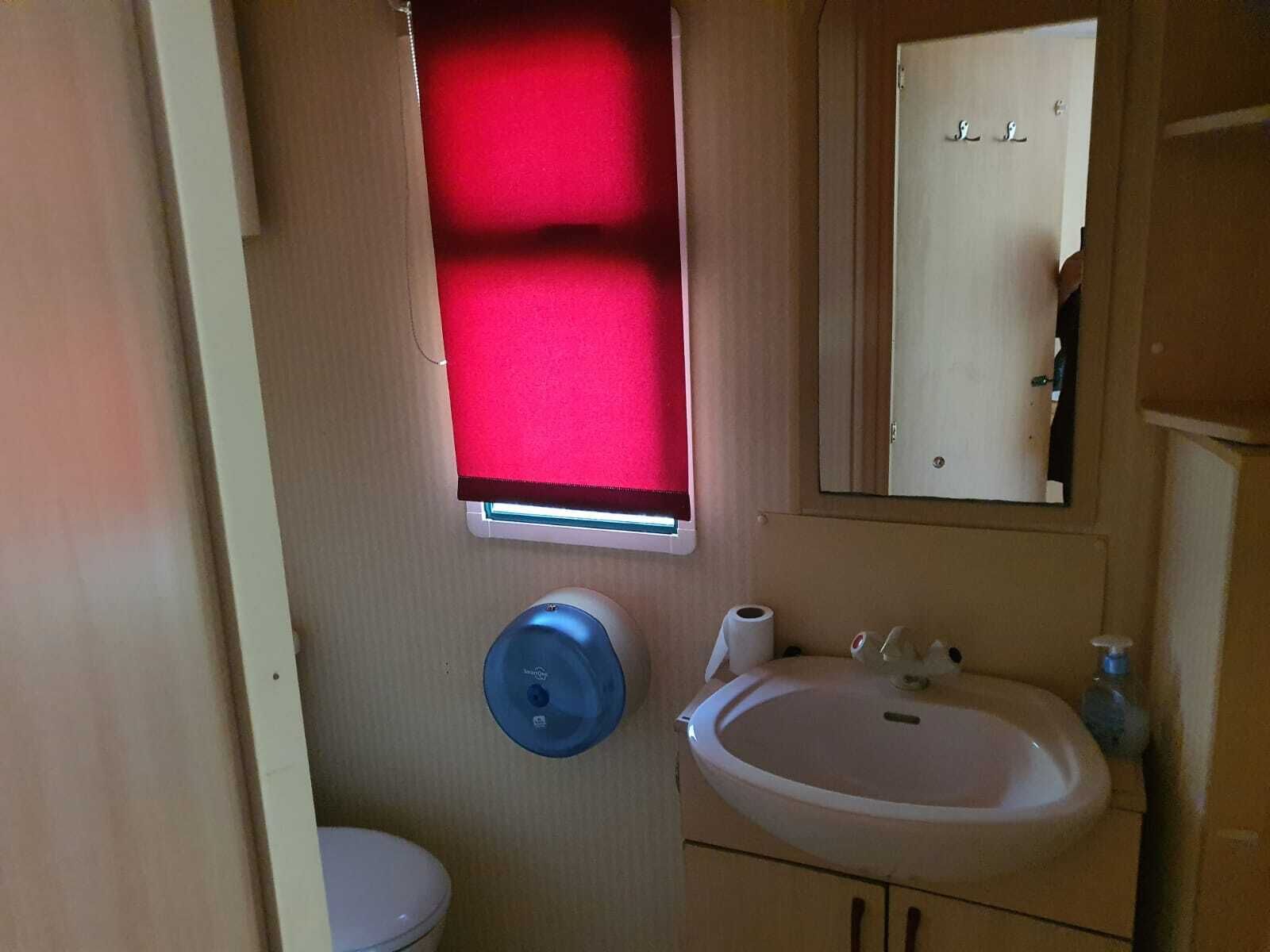 Un bany compacte amb vàter, rentapel i mirall, i una finestra amb to vermellós.