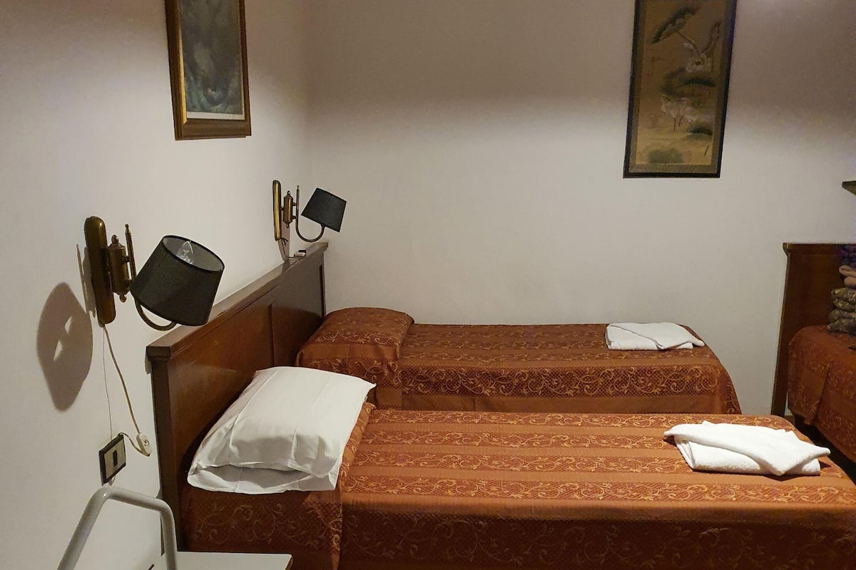 Ein Hotelzimmer mit zwei Betten, einem Schreibtisch, einem Stuhl, einem Koffer und einer Lampe.