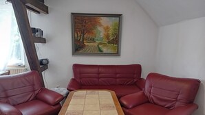 Un salon avec une table basse en bois, deux canapés en cuir rouge et un tableau représentant un paysage accroché au mur.