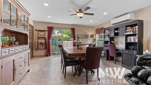 A spacious dining area with a wooden table and chairs, a ceiling fan, and a view of the outdoors through a glass door.