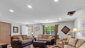A living room with two sofas, a coffee table, and a lamp. There is a door and a window with curtains.