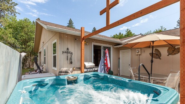 A hot tub in a backyard with a wooden pergola, a barbecue grill, and outdoor furniture.