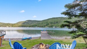 A lakeside deck with two blue chairs, a fire pit, and a dock extending into the water.
