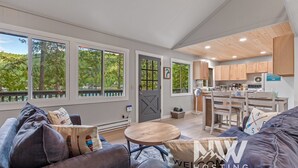 A spacious living area with a large sofa, a round coffee table, and a view of a deck through large windows.