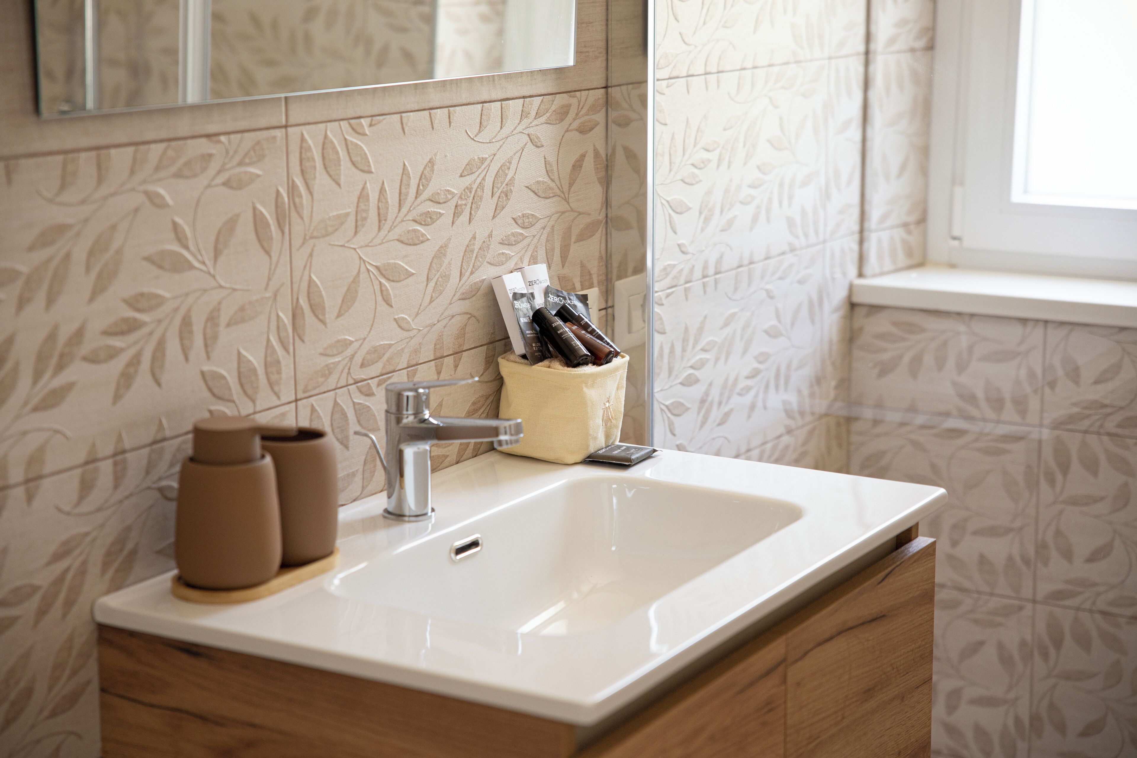 A bathroom with a white sink, a mirror above it, and a window to the right.