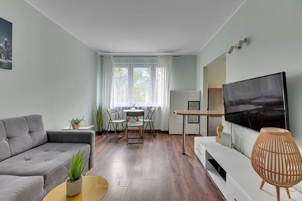 Ein modernes Wohnzimmer mit einem grauen Sofa, einem kleinen runden Tisch, einem Fernseher und einer dekorativen Lampe.