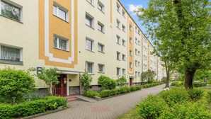 A multi-story residential building with a brick pathway and greenery. - RentPlanet - Apartament Piastowska (Gdansk)
