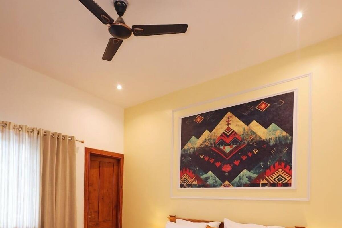 A bedroom with a wooden bed, a ceiling fan, a painting on the wall, and a wooden door.