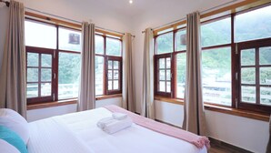 Une chambre d’hôtel avec un grand lit, deux fenêtres avec des rideaux et une vue sur la verdure.