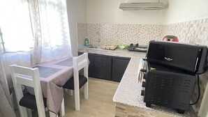 Een kleine keuken met een eettafel, stoelen, een grill en een spoelbak.