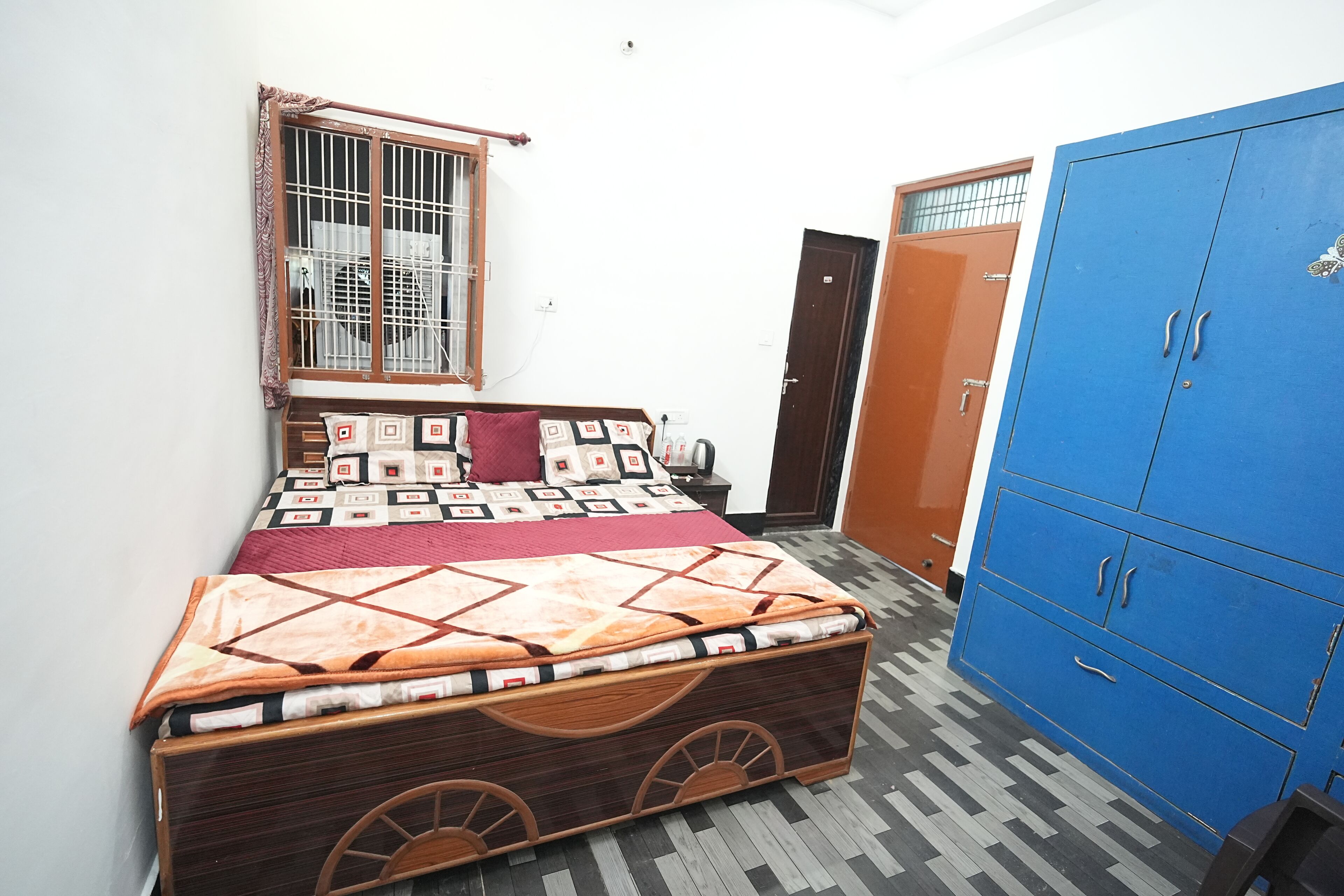 A bedroom with a bed, a wardrobe, and a window with bars.