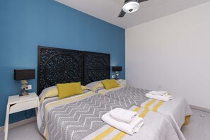 A bedroom with two beds, a ceiling fan, and a nightstand with a lamp. - Andalucia 5 - One Bed (Costa Adeje)