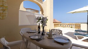 A dining table set with plates, cutlery, and a vase of flowers, with a view of the sea in the background. - Andalucia 5 - One Bed (Costa Adeje)