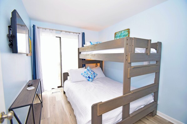 Una cama litera con ropa blanca, una mesita con un control remoto y un espejo en la pared.