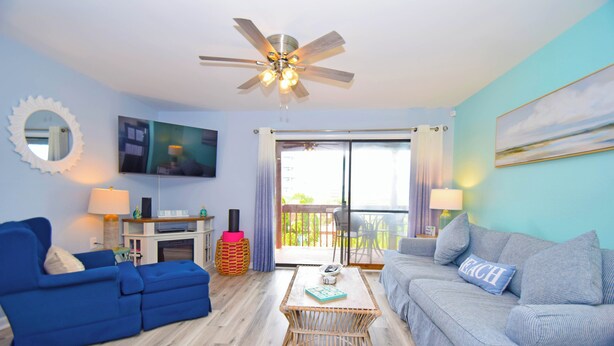A living room with two sofas, a coffee table, a ceiling fan, and a large window with curtains.