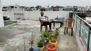 Un hombre sentado en un balcón con plantas en macetas y un ordenador portátil.