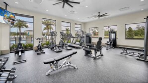 Een sportschool met diverse fitnessapparaten, grote ramen en een plafondventilator.