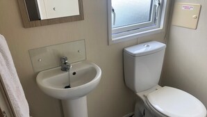 A bathroom with a white sink, toilet, and a window. - Seaside 2-bed Caravan Retreat - Sleeps 6 & Parking (Prestatyn)