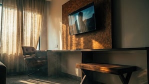 A modern room with a mounted TV, a wooden bench, a leather chair, and a large window with curtains. - Monarch Express, Sri City (Tada)