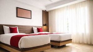 A hotel room with two beds, a ceiling fan, a framed picture on the wall, and a window with sheer curtains. - Monarch Express, Sri City (Tada)