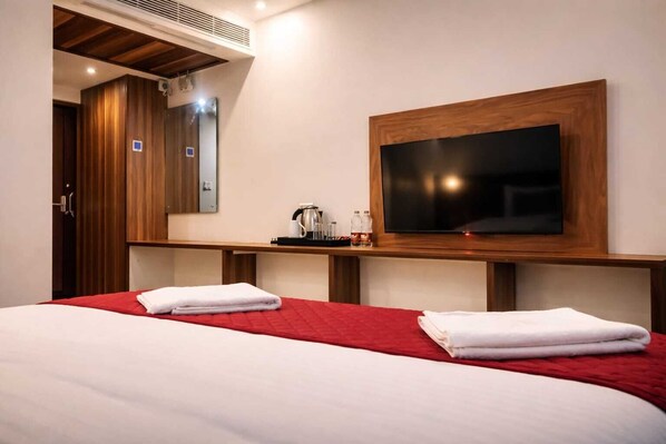 A hotel room with a large bed, a flat-screen TV mounted on the wall, a wooden desk, and a mirror. - Monarch Express, Sri City (Tada)