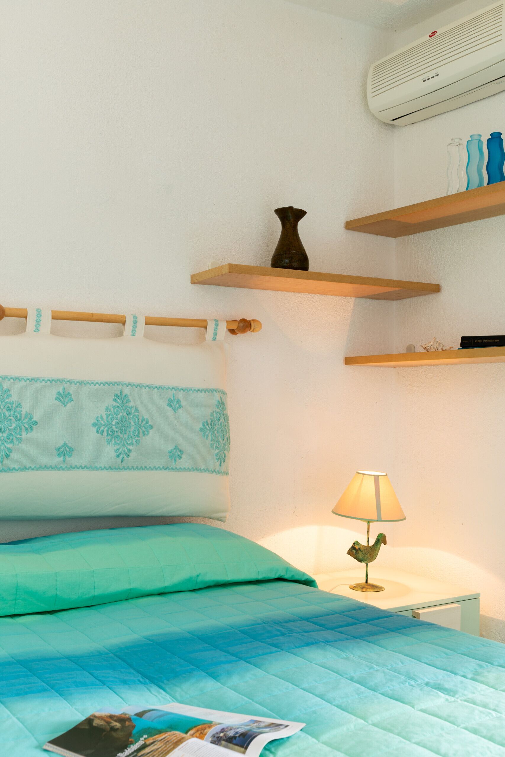 Un dormitorio con una cama, una lámpara de noche y una repisa con objetos decorativos.