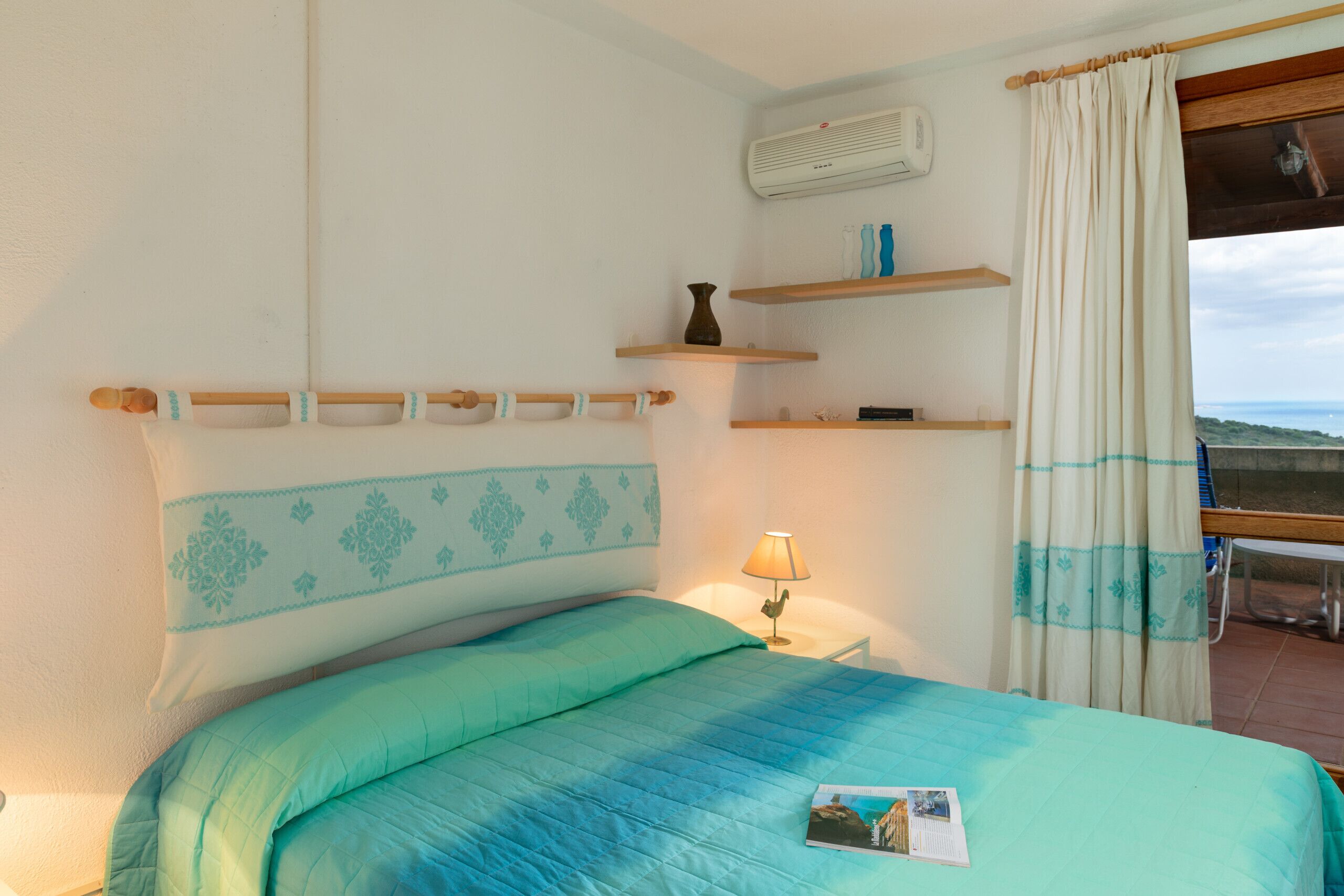 Une chambre à coucher avec un lit, une lampe de chevet, une fenêtre avec des rideaux et une vue sur l’extérieur.