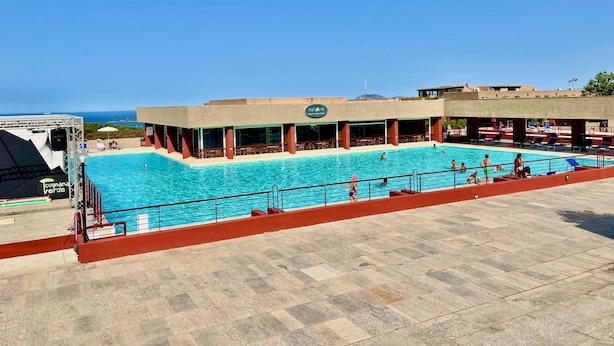 A swimming pool with a view of the ocean, a covered seating area, and a building with a sign. - Casa Sunrise by Wonderful Italy (Olbia)