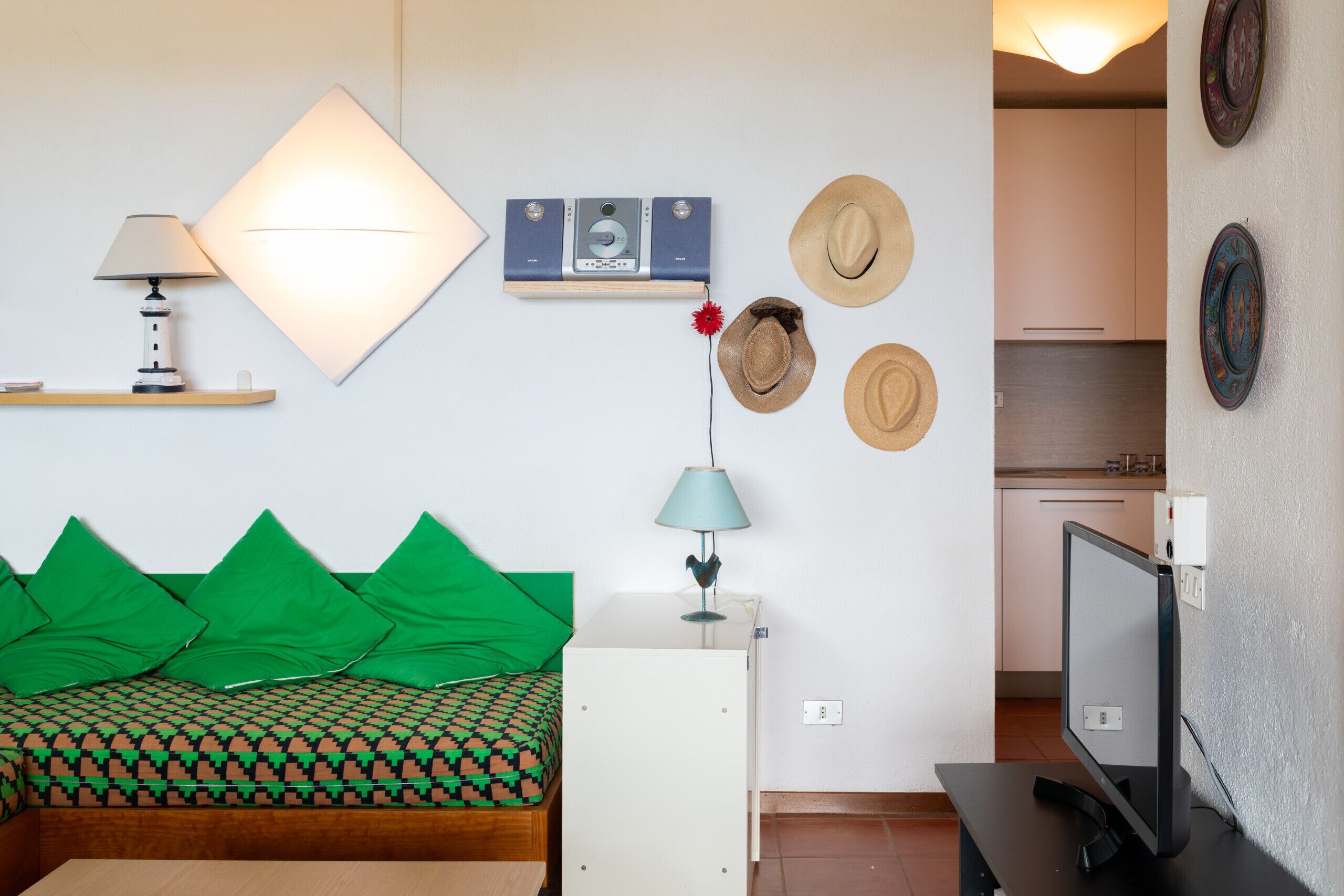 Ein modernes Zimmer mit einem Bett, einem Schreibtisch, einer Lampe, einem Fernseher und einem Wandregal mit Hüten und einer Kamera.