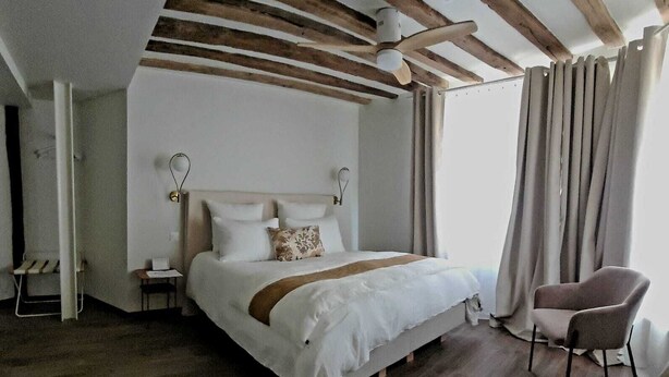 A bedroom with a large bed, wooden beams on the ceiling, a chair, and a nightstand. - 4 Charming Suites & downtown (Sens)