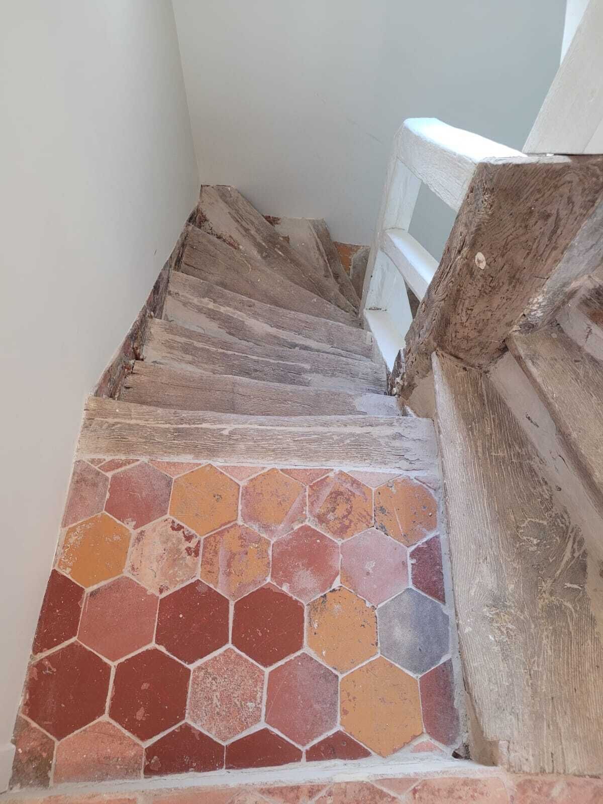 A staircase with a wooden handrail and a tiled floor with a hexagonal pattern.