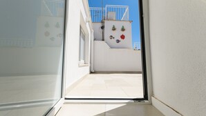 Un pasillo estrecho que conduce a un balcón con baranda blanca y suelo de baldosas.