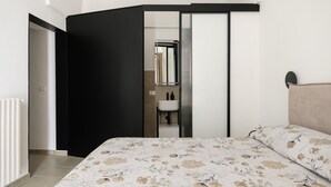 Een slaapkamer met een bed, een zwarte garderobe, een badkamer met een spiegel en een radiator.