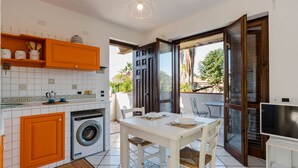 A compact kitchen with a washing machine, a dining area with a table and chairs, and a sliding glass door leading to an outdoor area. - Margiù Capomulini Home by Wonderful Italy (Acireale)