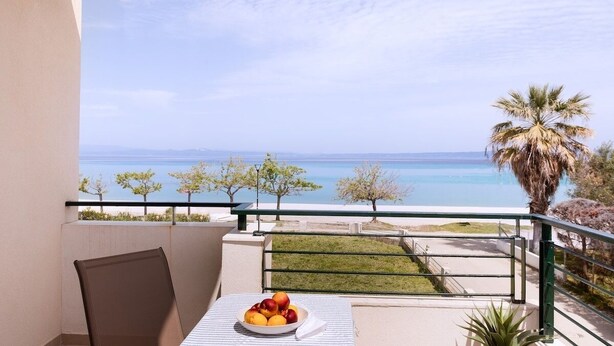 Un balcon avec une table dressée pour le petit-déjeuner, offrant une vue sur la côte, avec des palmiers et un ciel dégagé.