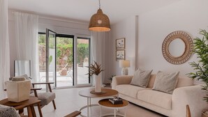 Un salon moderne avec un canapé, une table basse et des fauteuils. On y trouve une grande fenêtre avec des rideaux, un luminaire suspendu et un miroir fixé au mur.