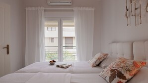 A hotel room with two beds, a window with curtains, an air conditioning unit, and a view of the outside. - Paradise Overlook - Beachfront Villa (Pefkohori)